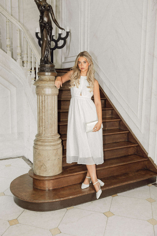 Woman in a white dress standing on a staircase in an elegant interior setting