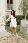 Woman in a white dress standing in an elegant outdoor setting with classical architecture.