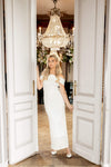 Woman in a white dress standing in a doorway with a chandelier above.