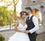 Couple in wedding attire standing in front of a stone archway.