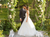 Couple in wedding attire standing under a floral archway with candles on a wooden platform.