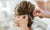 Person adjusting a hairpiece in a styled updo with a blurred background