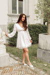 Woman in a white dress standing outdoors near a building with greenery.