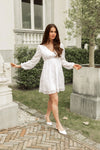 Woman in a white dress standing outdoors near a classical building.