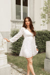 Woman in a white dress standing in front of a classical building with columns.