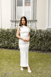 Woman in a white dress standing on grass with a building and hedge in the background