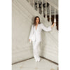 Woman in a white suit standing on a staircase with white walls and wooden banisters.
