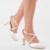 White high-heeled shoes with thin straps worn by a person on a light gray background